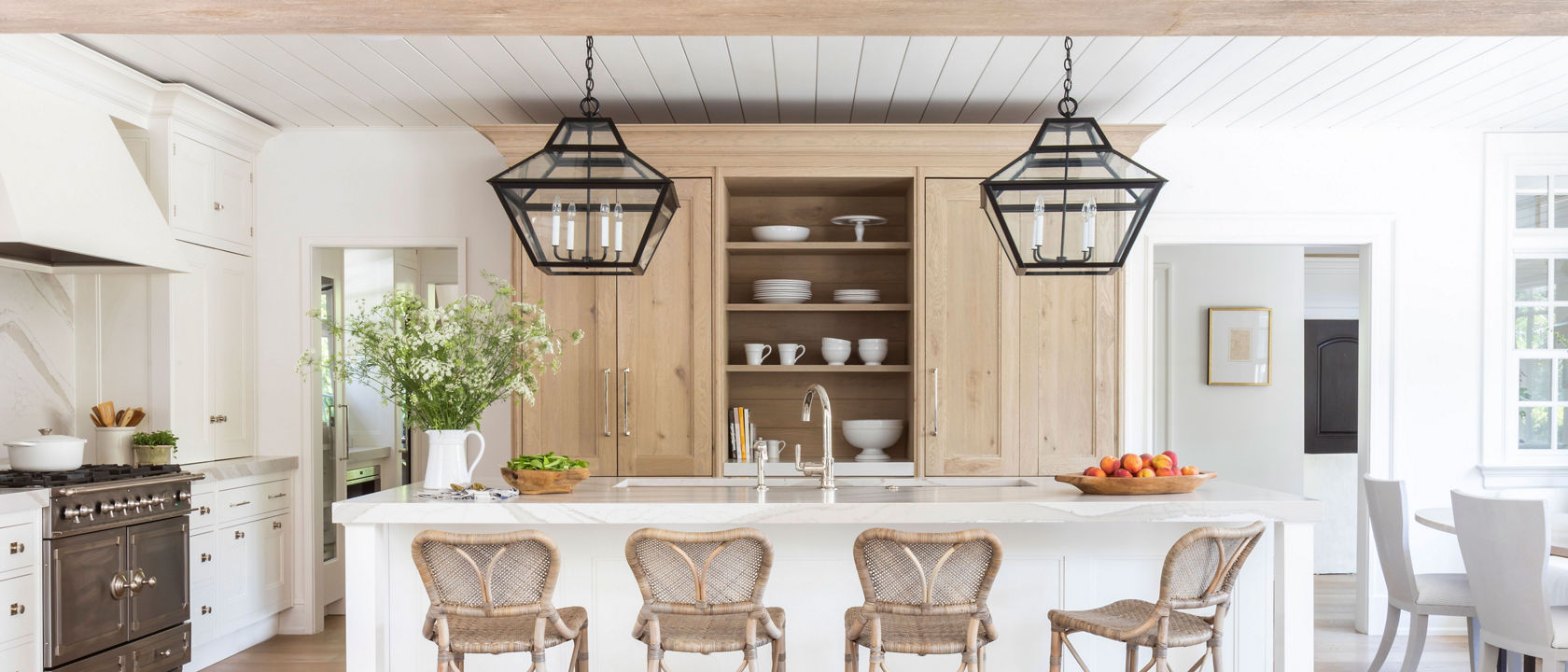 a modern farmhouse inspired kitchen with white and oak cabinets, a modern range and hood, open shelving, a white quartz veined backsplash, countertops, and island, and black pendant light fixtures. 