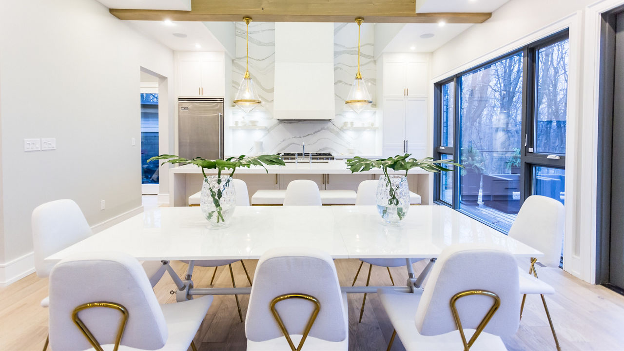 A luxurious modern kitchen with a full-height quartz backsplash, double waterfall-edge island, a white table with white and gold tables, and lots of natural light. 