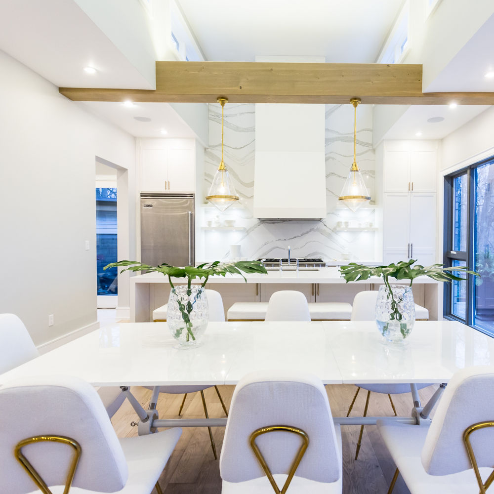A luxurious modern kitchen with a full-height quartz backsplash, double waterfall-edge island, a white table with white and gold tables, and lots of natural light. 