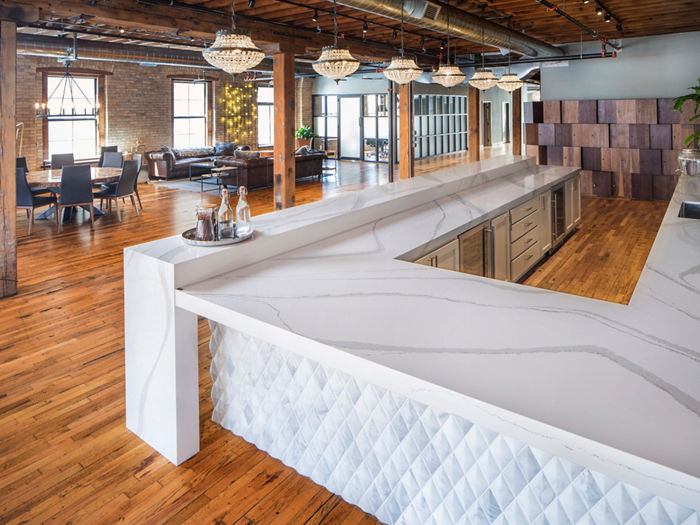 an industrial bar with exposed bricks, metal pipes on the ceiling, various tables and seating arrangements, oak floors, and a white, modern bar with white quartz countertops.