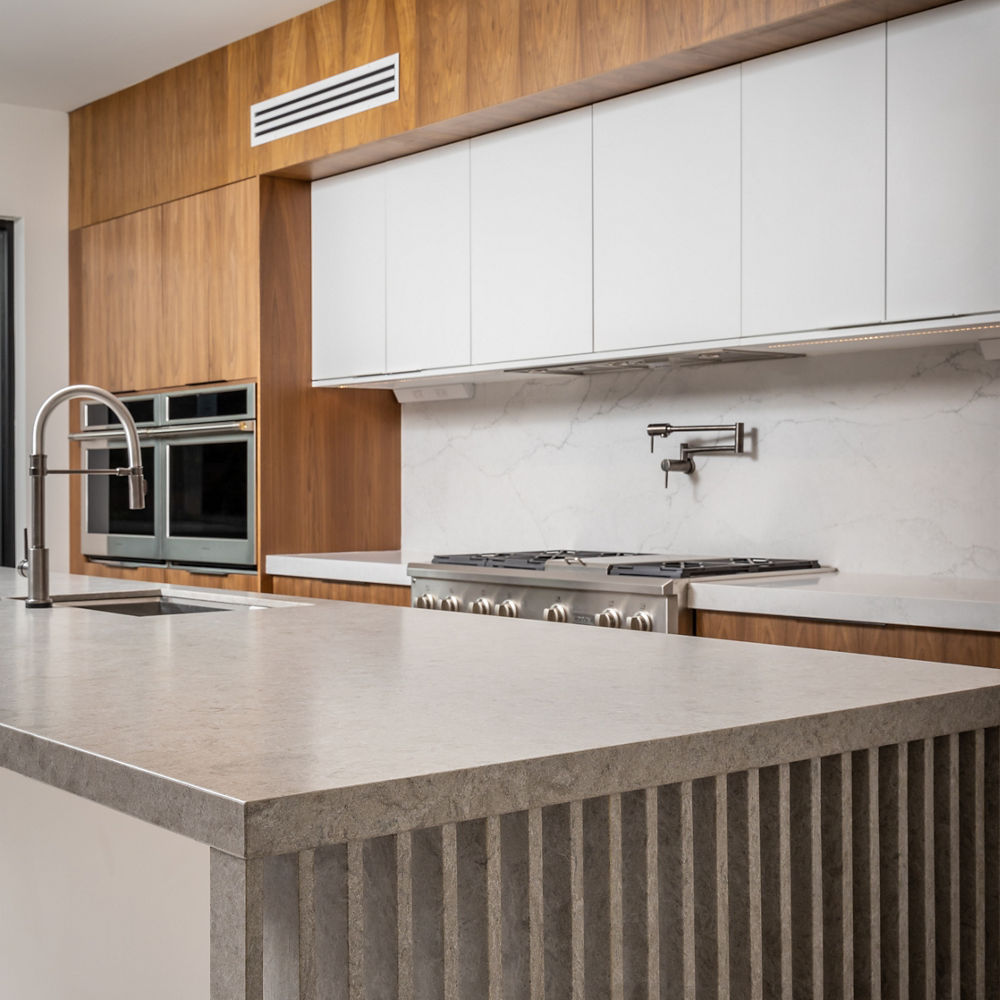 A gray kitchen with wood paneling on cabinets and the overhead wall with a gray island with pillars along its siding.
