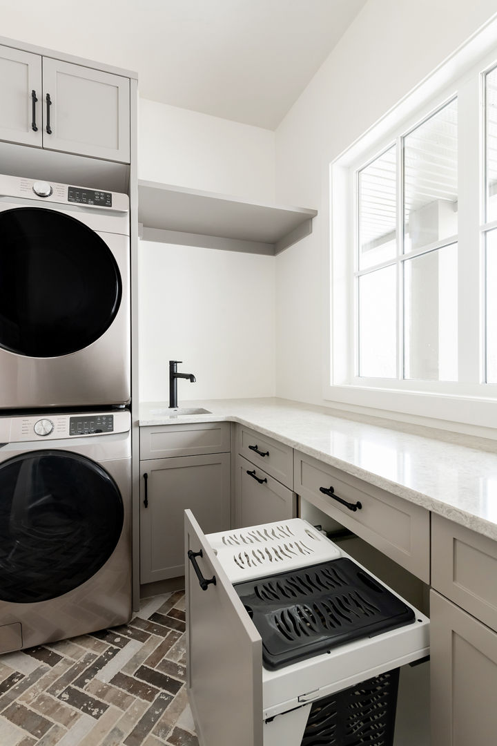 a clean laundry room with herringbone tiled flooring, gray cabinets, and white quartz countertops.