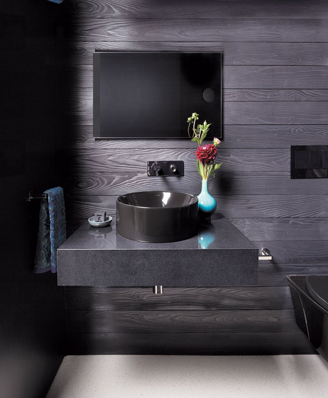 A dark and elegant powder bathroom with a black quartz floating vanity, black shiplap walls, a black sink, and various decorations.
