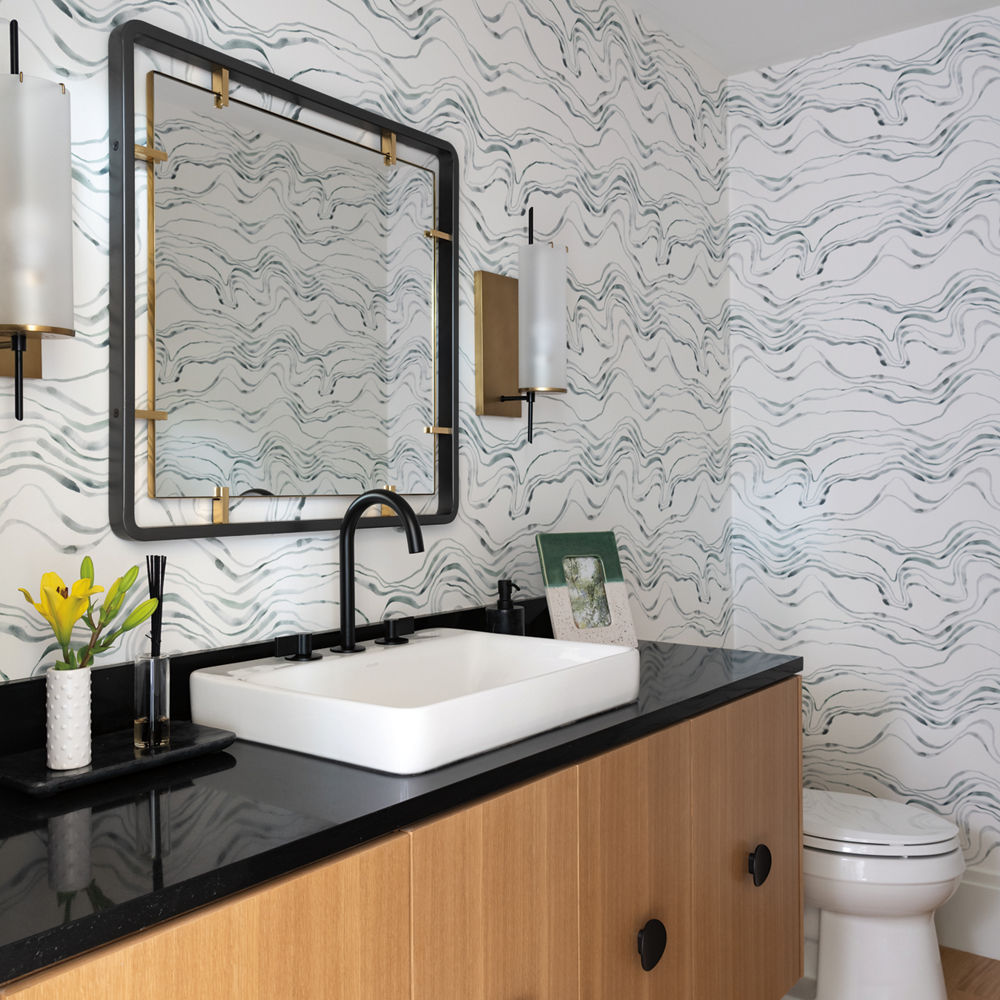 a bathroom with a semi-floating vanity made from oak with black handles, black quartz countertop, white sink, and black and gold mirror. 