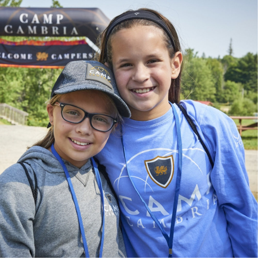Photograph of two girls wearing Camp Cambria apparel in front of a Camp Cambria banner.