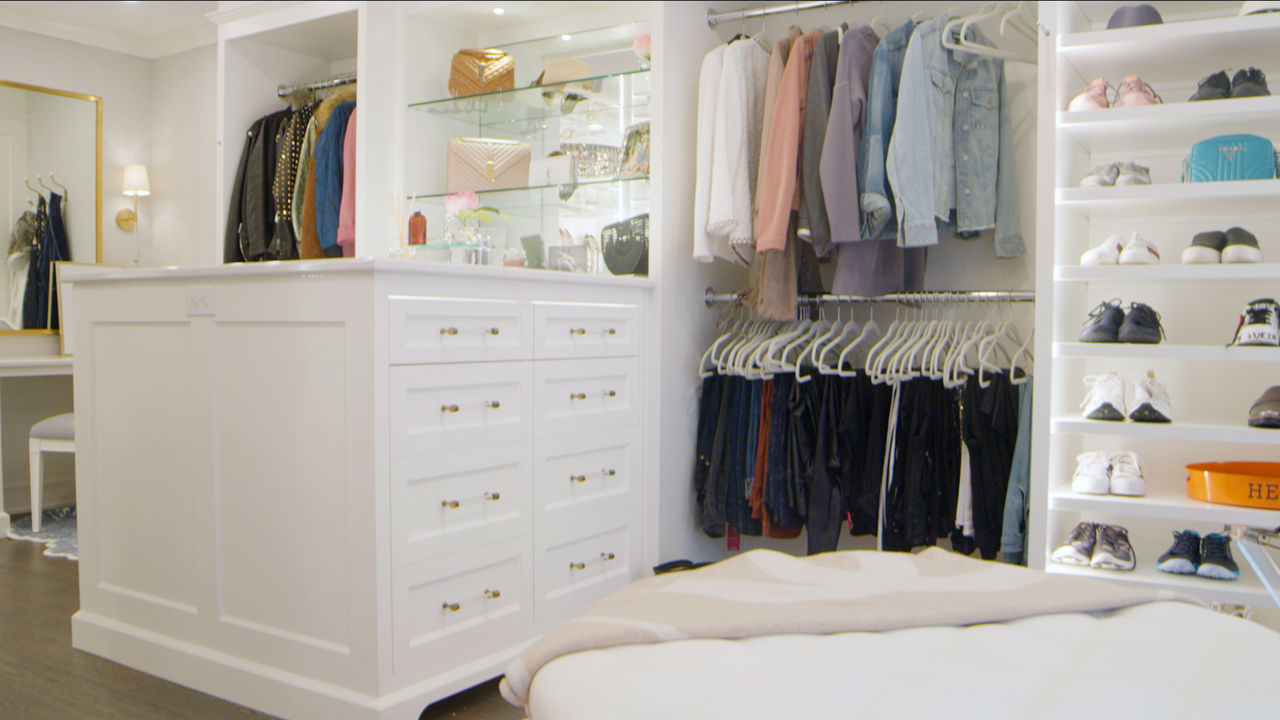 A walk-in closet with a focus on the clothes hanging in the closet and the displayed shoes and purses throughout the closet.