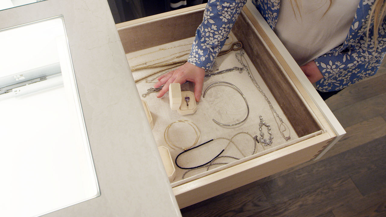 Display drawers containing various pieces of jewelry, as Carly Zucker's hand is around a ring display case.