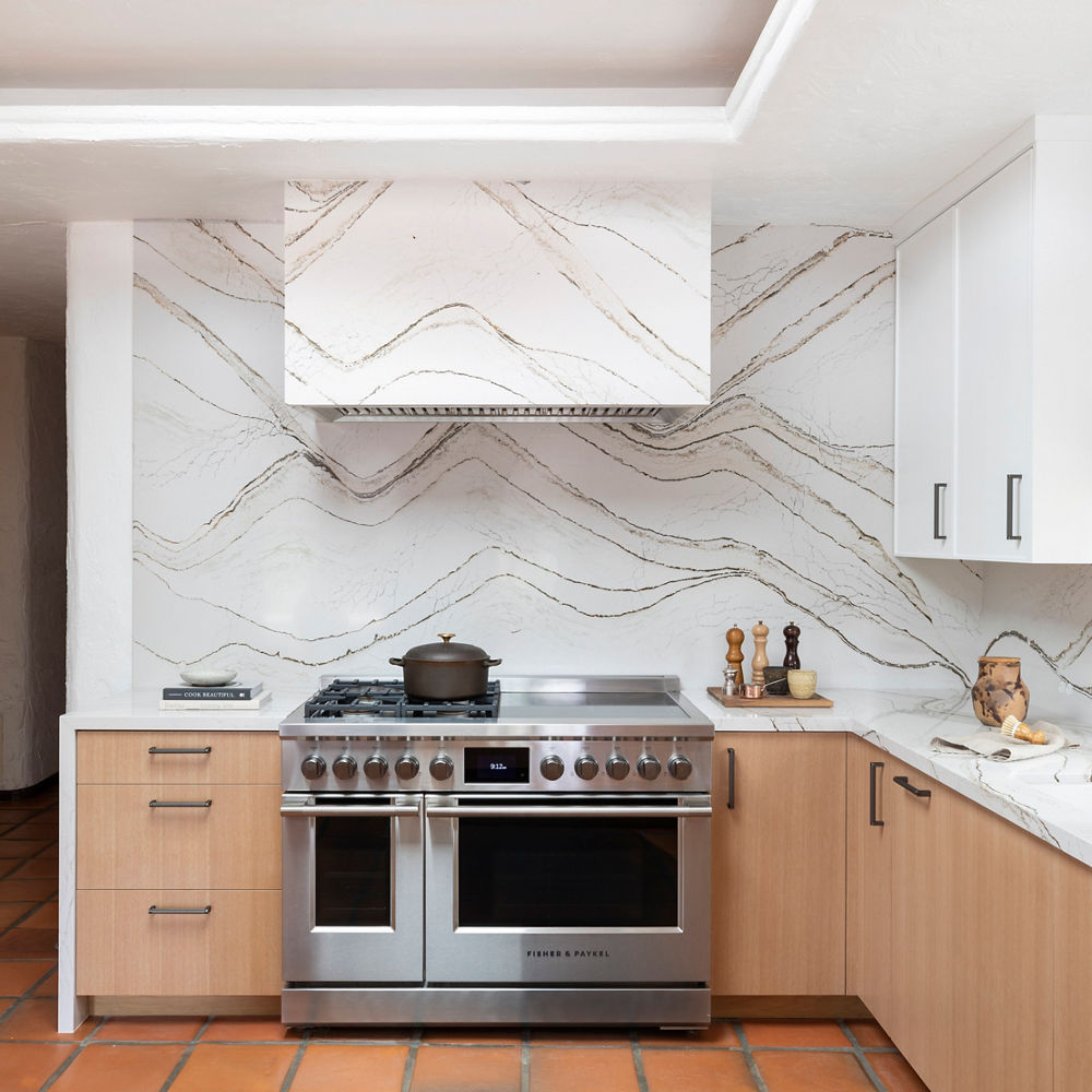 Kitchen with steel oven and stove surrounding a countertop and wall with Cambria Clovelly quartz.