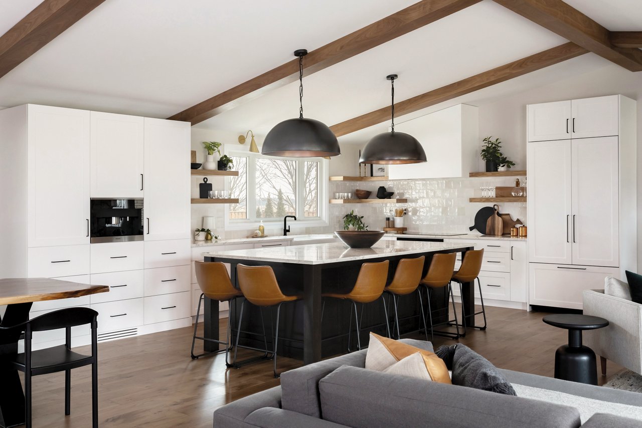 A kitchen with open wood shelving, vaulted ceilings with wooden beams, white cabinets and gorgeous center island with wooden barstools topped with Colton quartz countertops