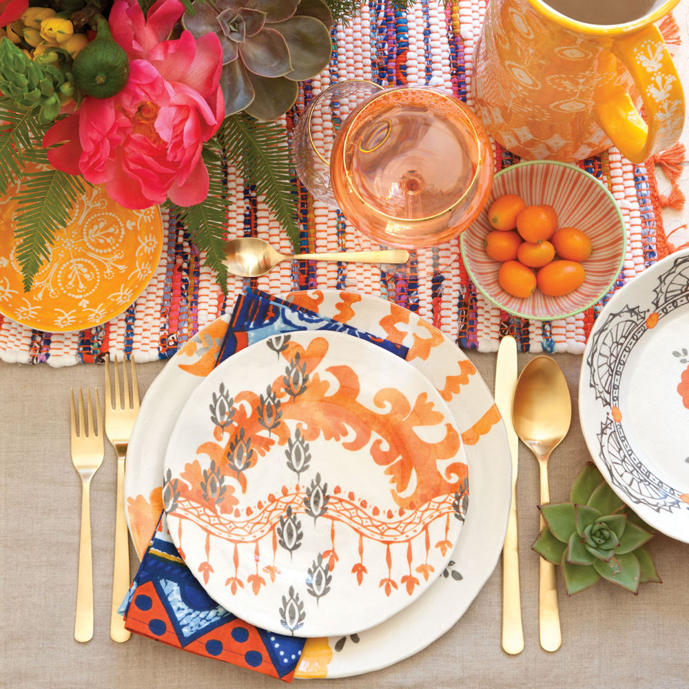 a tabletop set-up with a runner, chargers, flowers, and utensils.
