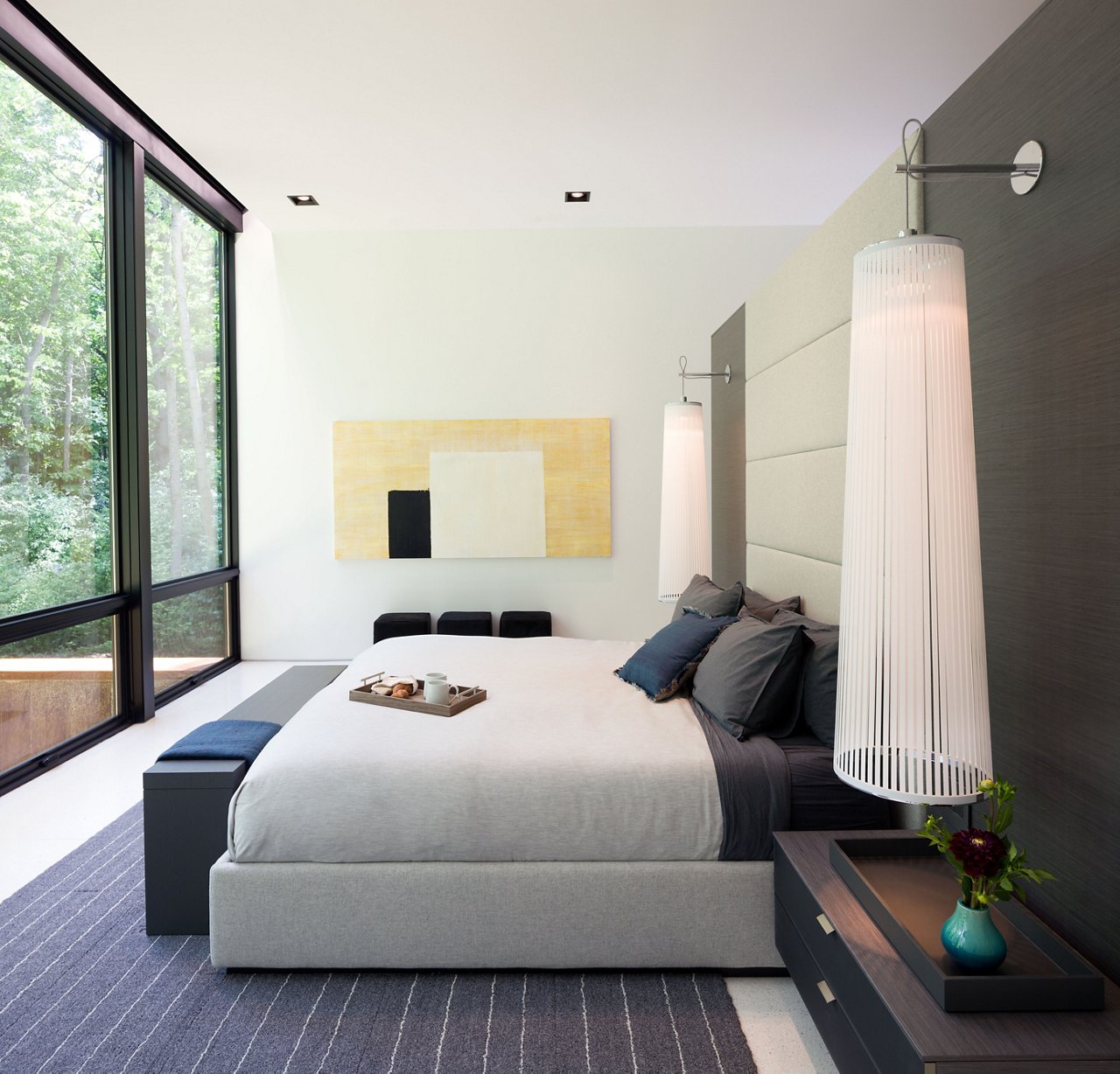 A master bedroom with a full wall of windows, and elegant wall lighting.
