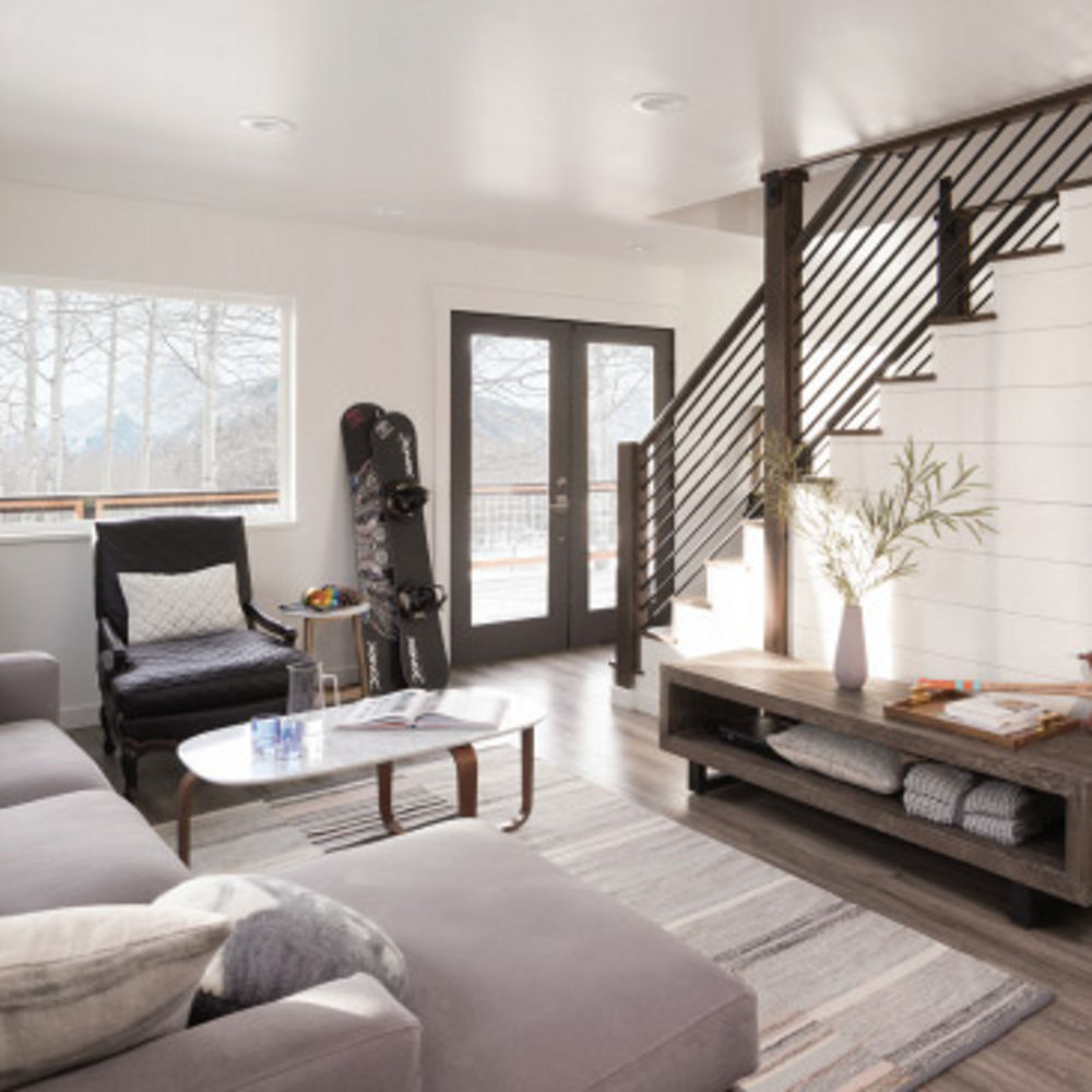 a warm living room with white shiplap on the wall by the stairs, gorgeous wooden floors, a greige couch, and white walls. 