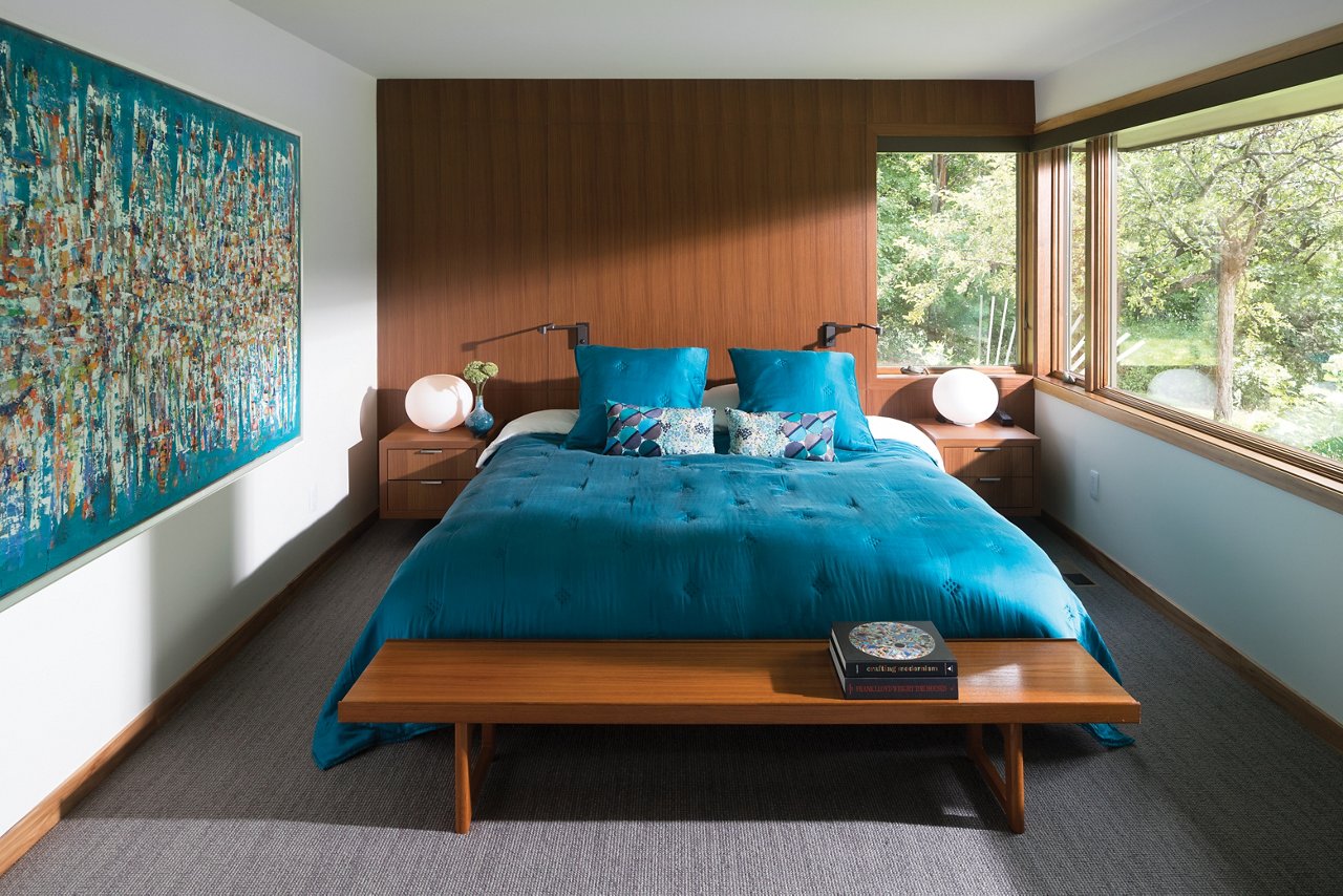 a mid-century modern bedroom with wooden paneling on one wall, a bed with teal comforter and pillows, and a bench.