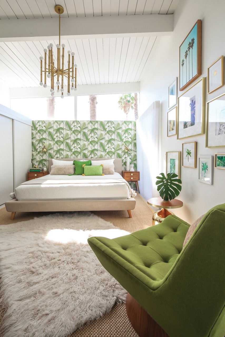 A mid-century modern bedroom with green accent wallpaper behind the bed, a shag carpet rug, and a green armchair.