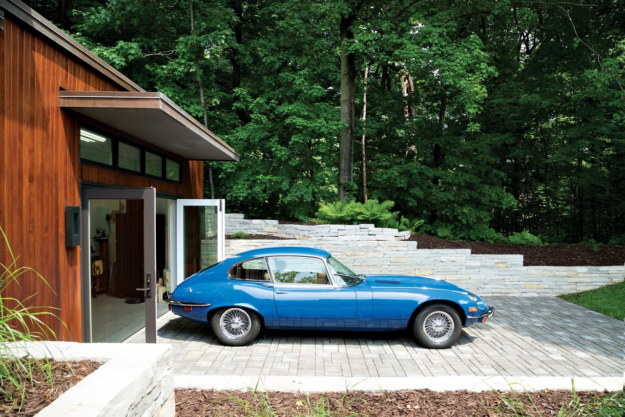 An old blue car outside a mid-century modern house.