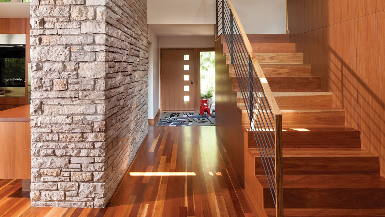 A front hall of a mid-century modern house featuring wooden flooring, a stone wall, and high windows. 