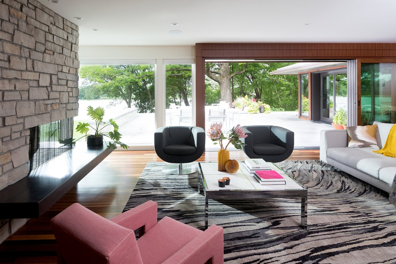 a mid-century modern living room with a stone fireplace, zebra pattern rug, pink chair and black chairs, and white couch.