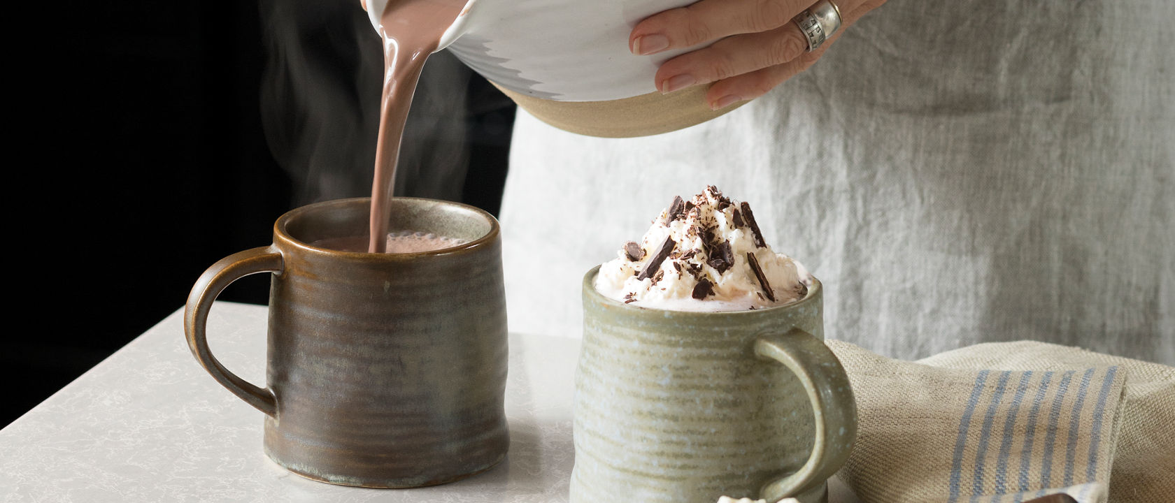 Hot chocolate being poured into a mug over a counter with a Cambria Big Sur Mist quartz countertop.
