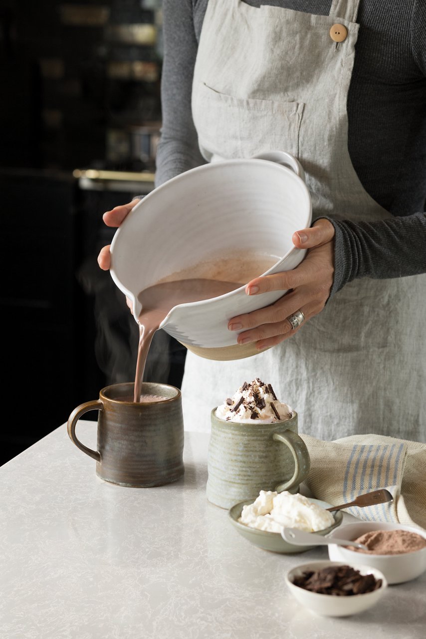 Hot chocolate being poured into a mug over a counter with a Cambria Big Sur Mist quartz countertop.
