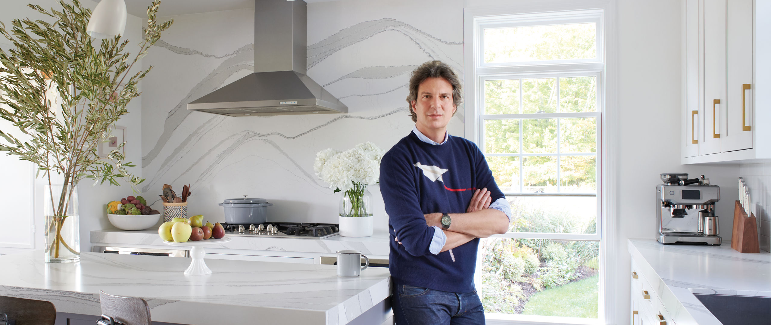 Adam Glassman standing in a white kitchen, leaning against an island with a white quartz countertop.