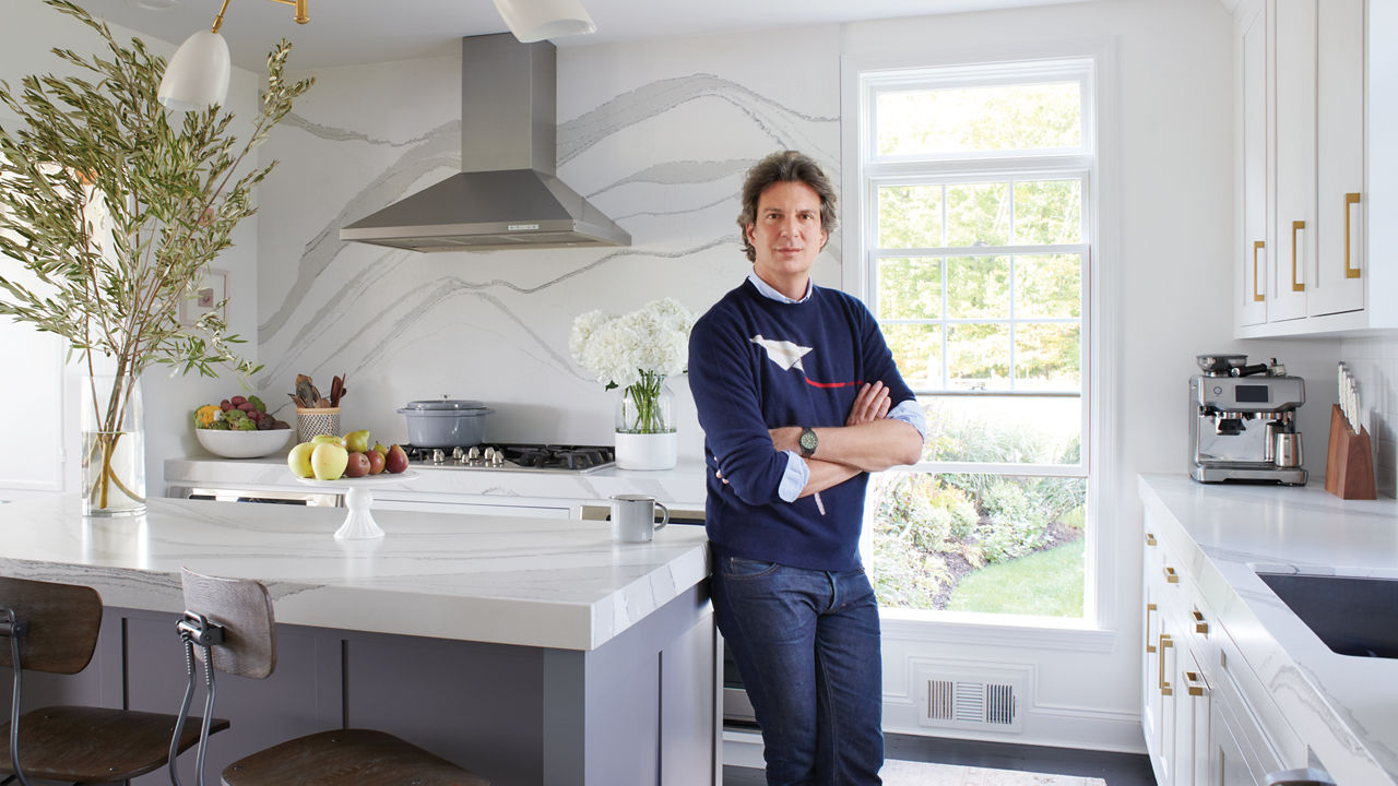 Adam Glassman standing in a white kitchen, leaning against an island with a white quartz countertop.