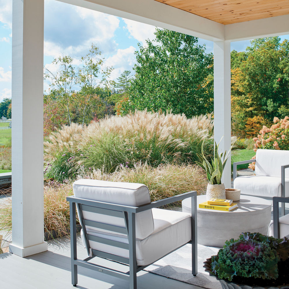 A home porch with three white chairs facing a circle table with rolling farmland in the background.