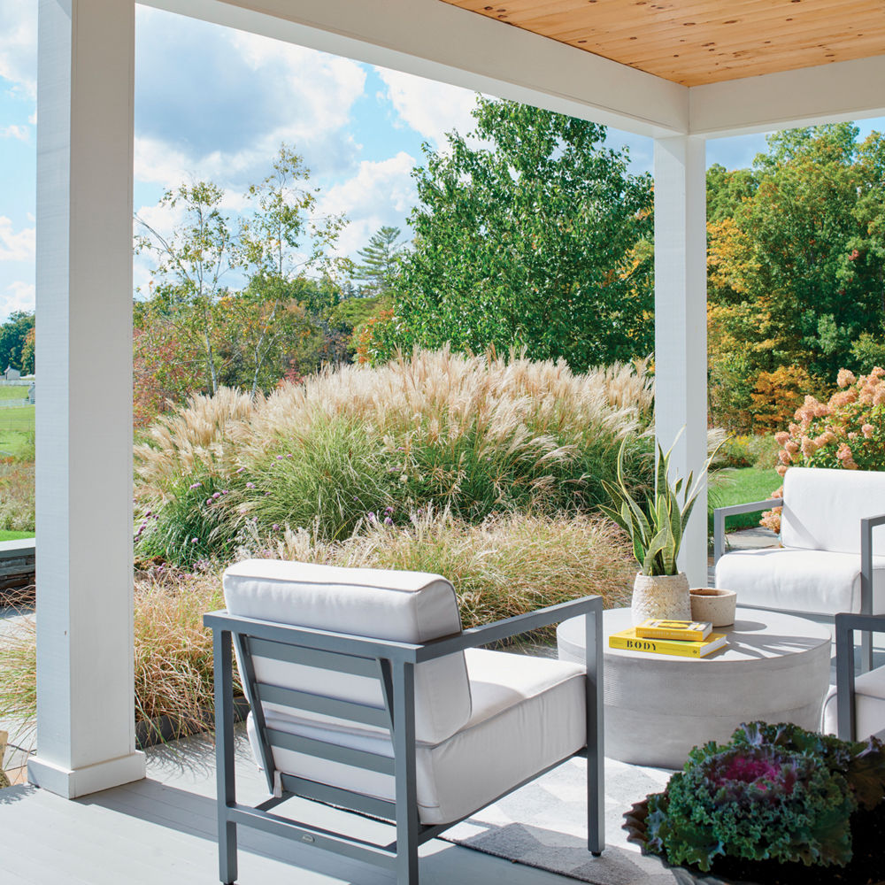 A home porch with three white chairs facing a circle table with rolling farmland in the background.