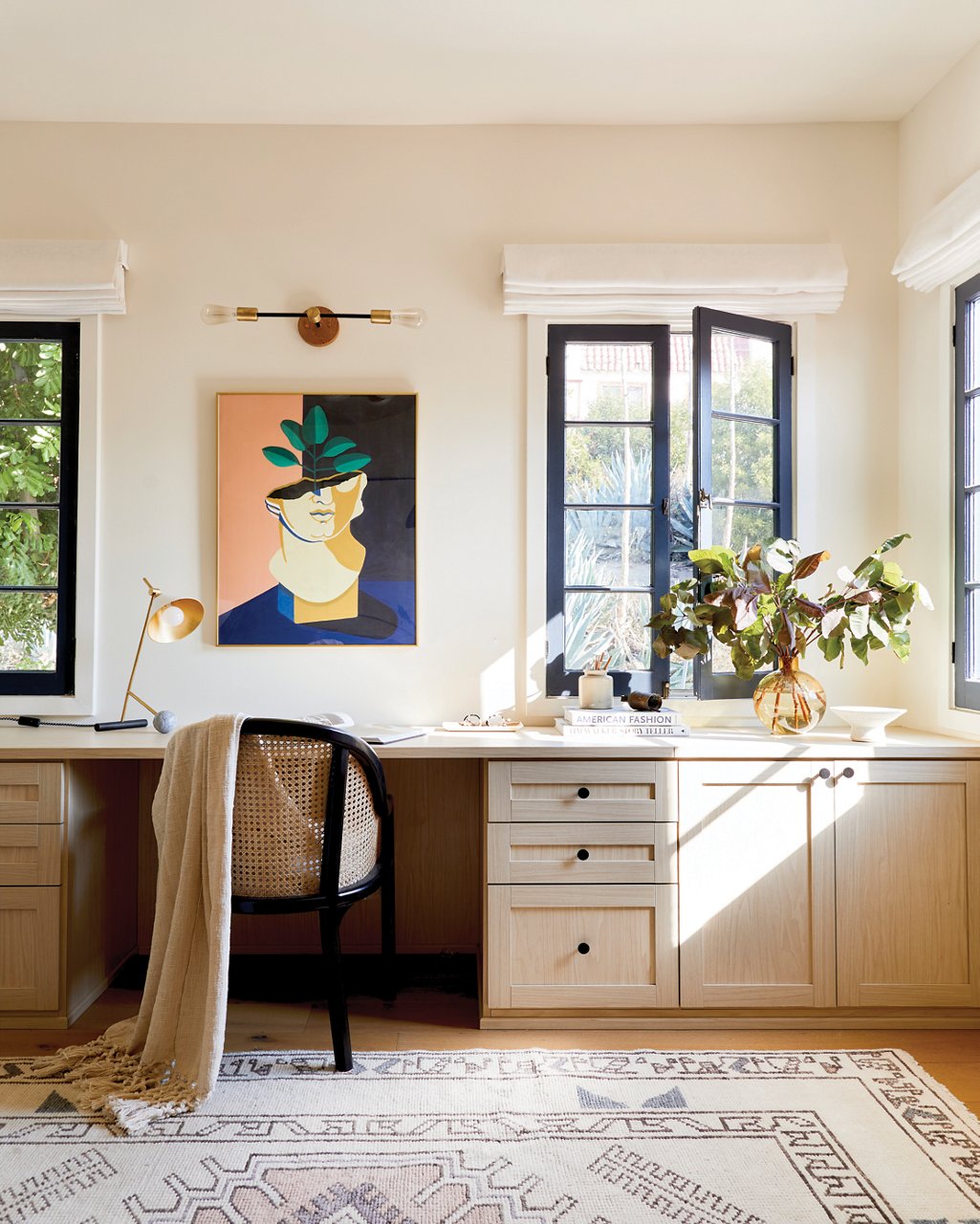 A desk inside of a Spanish-style home with an abundance of natural sunlight and an abstract painting on the wall.