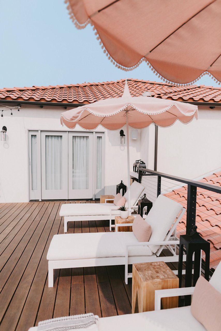 A brown deck with white patio chairs and pink umbrellas.