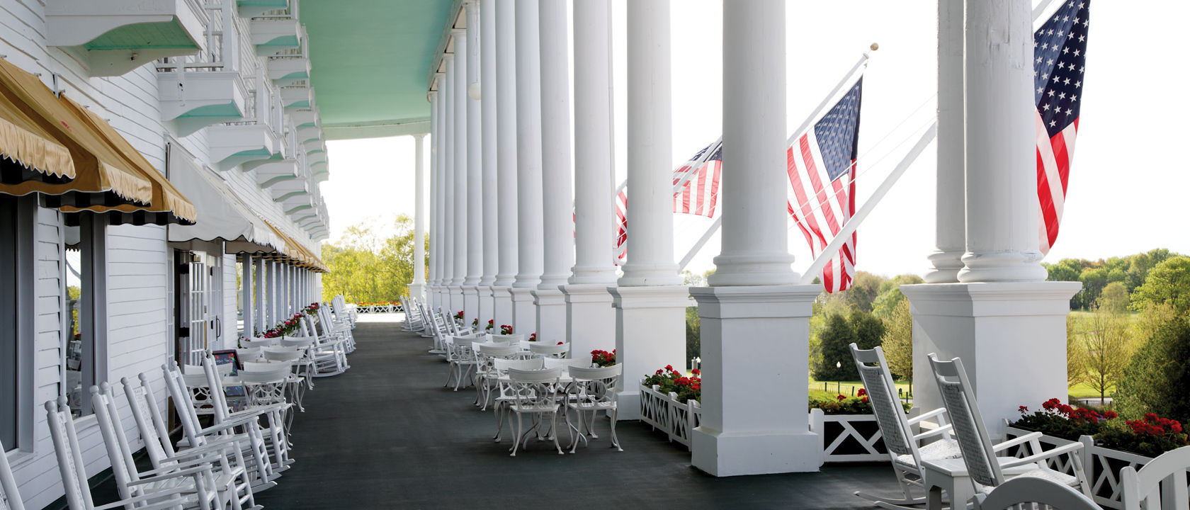The Grand Hotel's exterior patio with several tall columns with American flags hanging, and places to sit and look at the views.