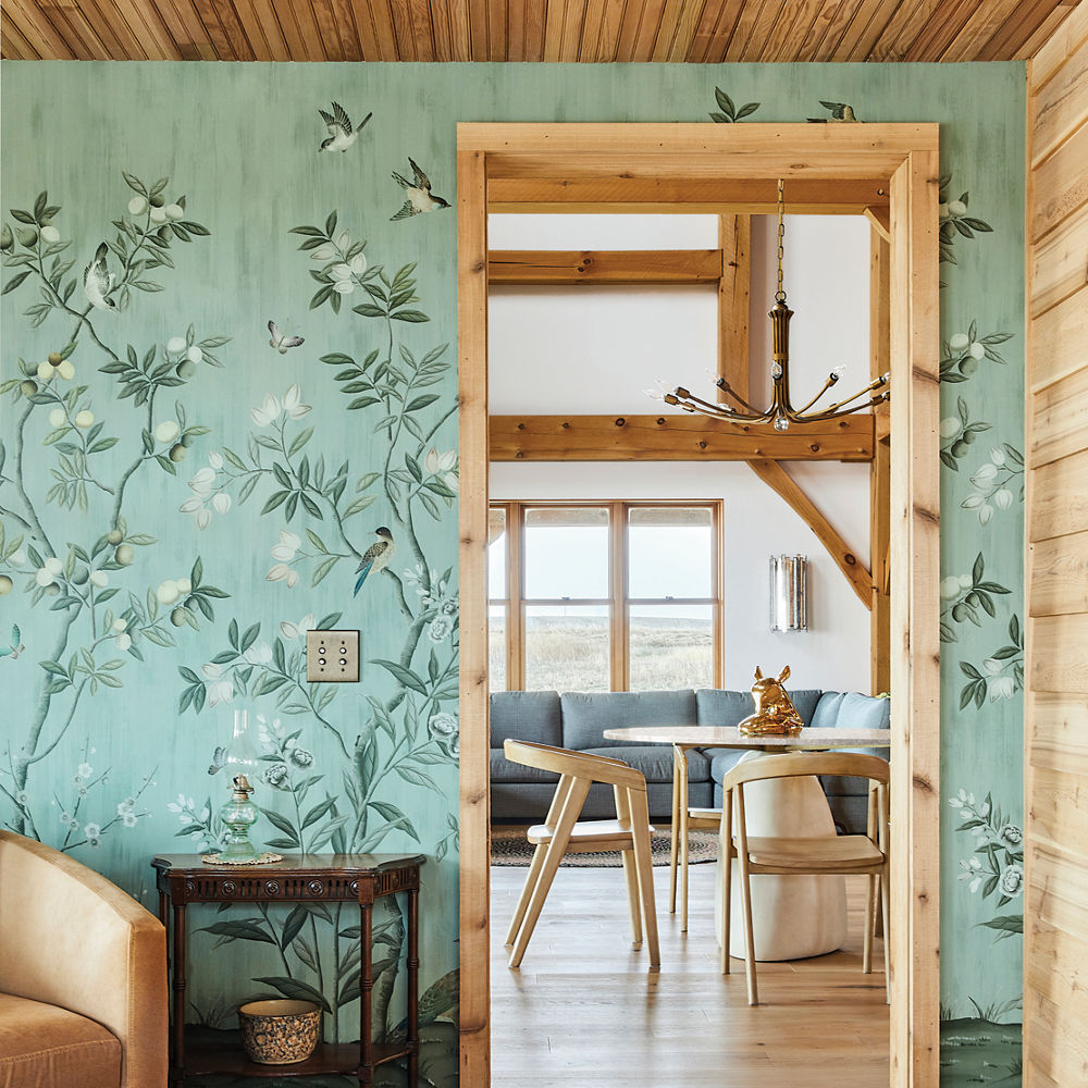 a living room with floral green wallpaper, wooden floors and ceilings, and a dining room with a quartz table.