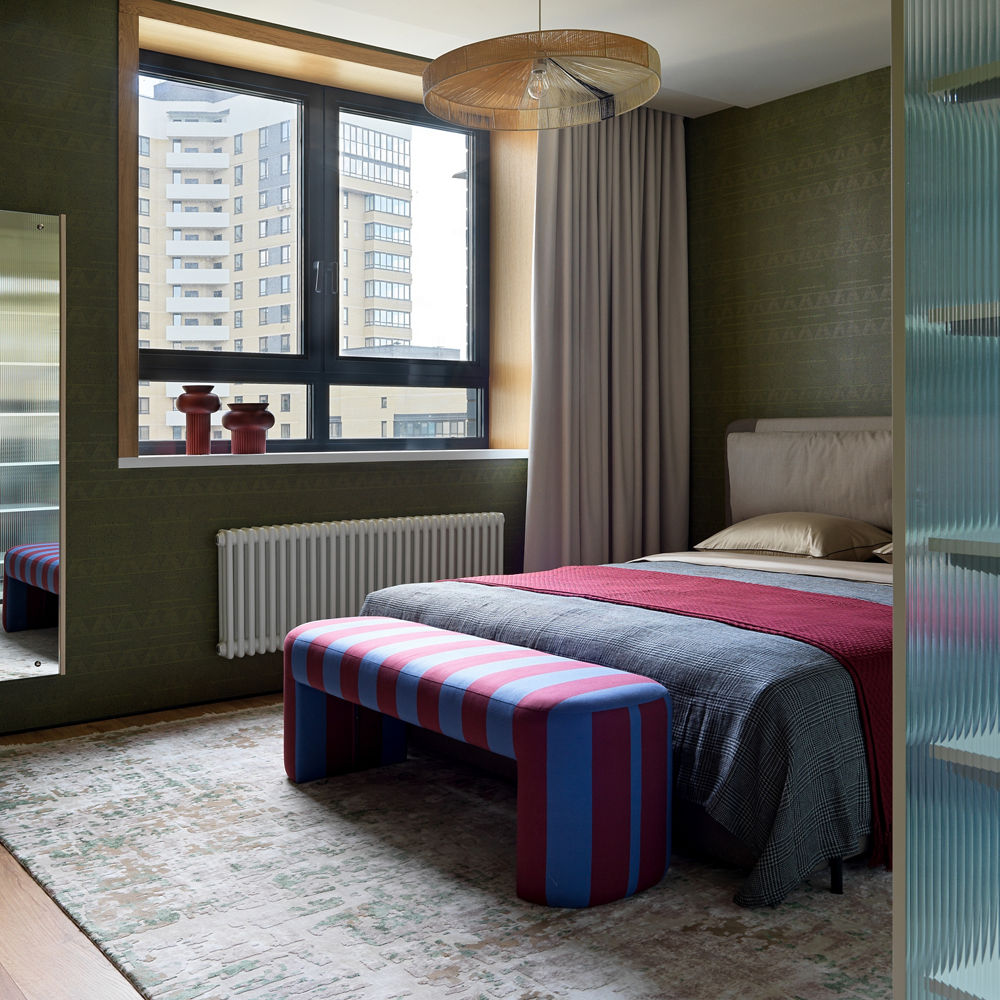 a master bedroom with colorful bedding, an ottoman, area rug, and overhead ceiling light.