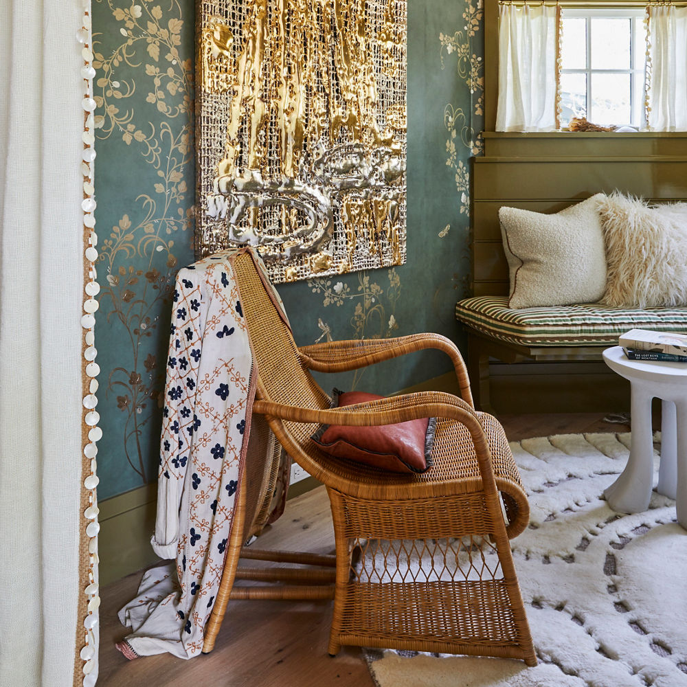 A seating area with green and gold wallpaper, a shiny gold piece of art hanging on the wall, and several seating options.