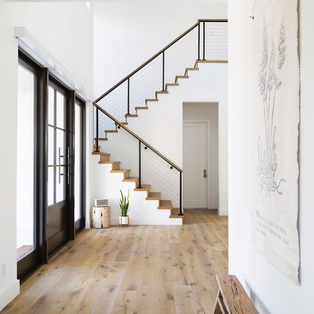 An entryway with gorgeous wooden floors, black door, and a staircase.