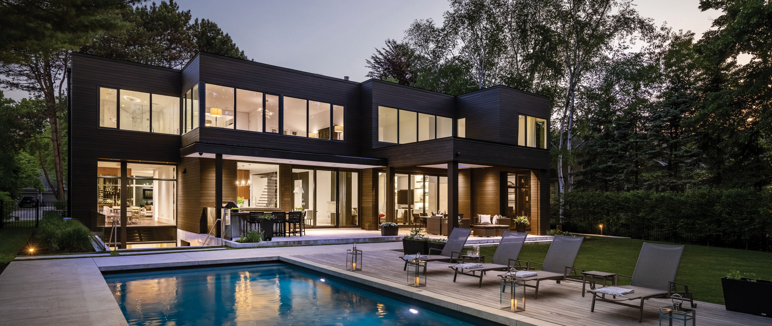 An exterior shot of a modern black home with a large outdoor pool. 