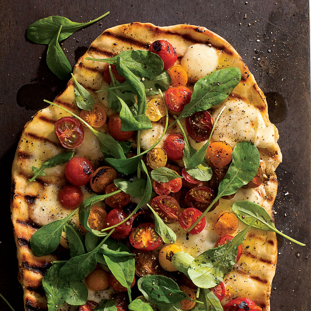 A pizza with arugula, cherry tomatoes, and mozzerlla.