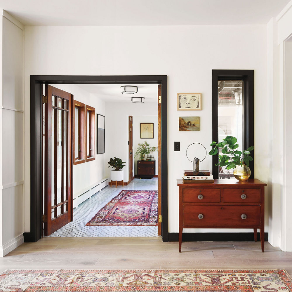 A hallway with a bookshelf, area rug, arch with black trim, and light wooden flooring