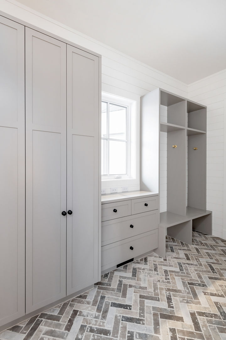 a laundry room storage area with floor-to-ceiling gray cabinets, two cubbies, and herringbone tiled flooring. 