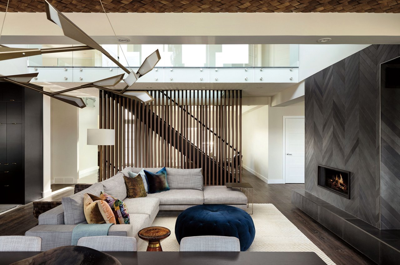 a luxurious living room with a fireplace, sectional couch, high ceilings, and a circular pouf ottoman.