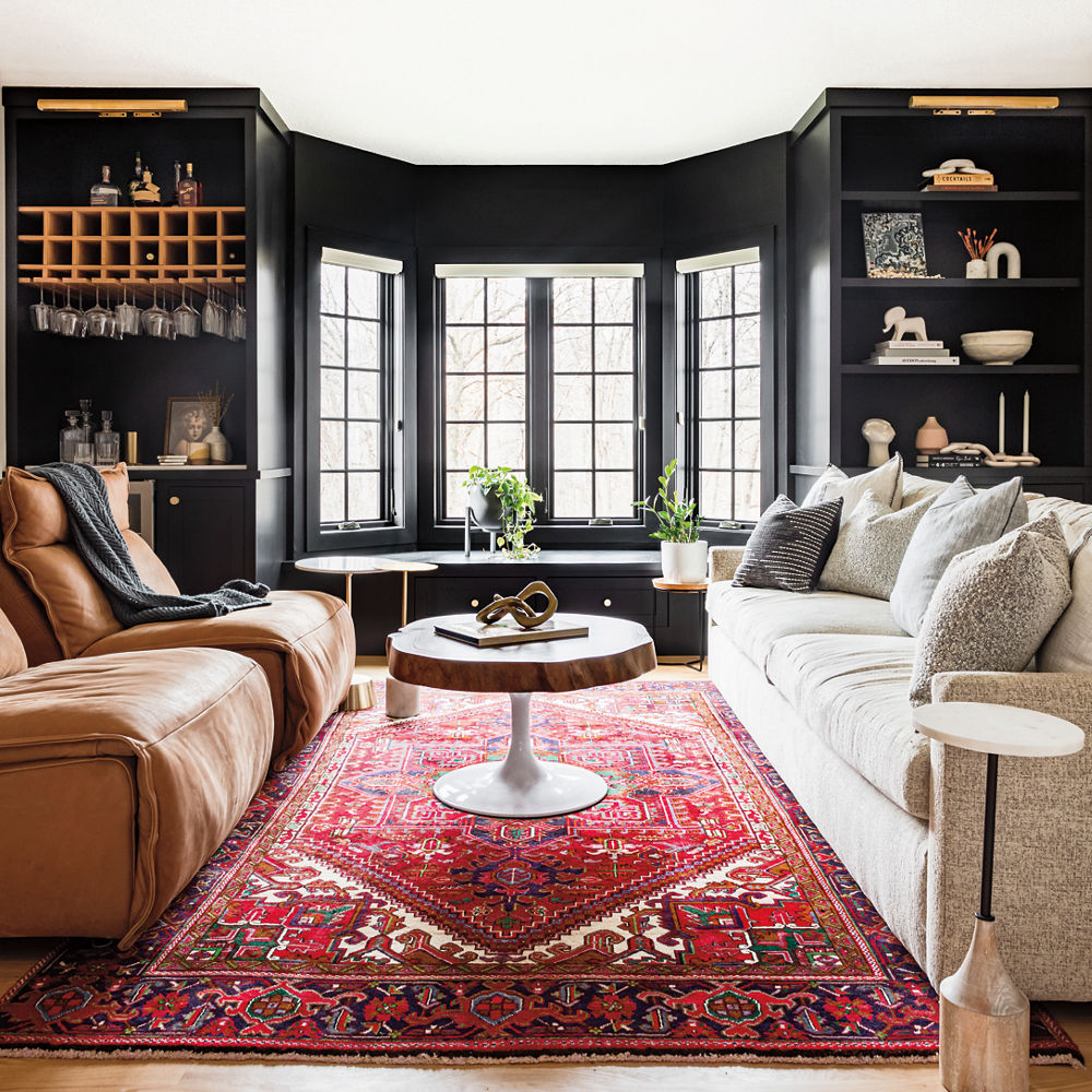 A living room with a colorful rug, dark painted walls, and a sitting nook