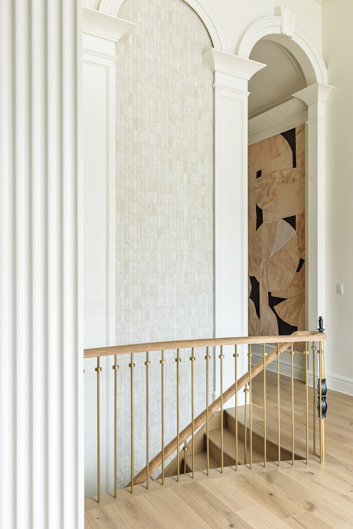 An archway at the top of the stairs is filled with Mosaico Nantes Caliza tile from Porcelanosa. The delicate stair rail is made of white oak and solid brass.