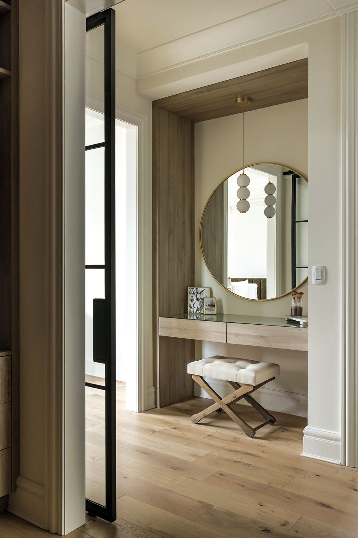 A beige dressing table in the corner of a bedroom, featuring a circular mirror and cushioned stool.