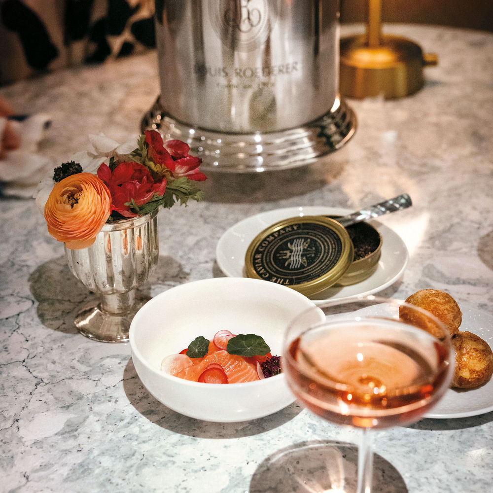 various plates with fruit and caviar, and a glass of champagne on top of a white quartz table.