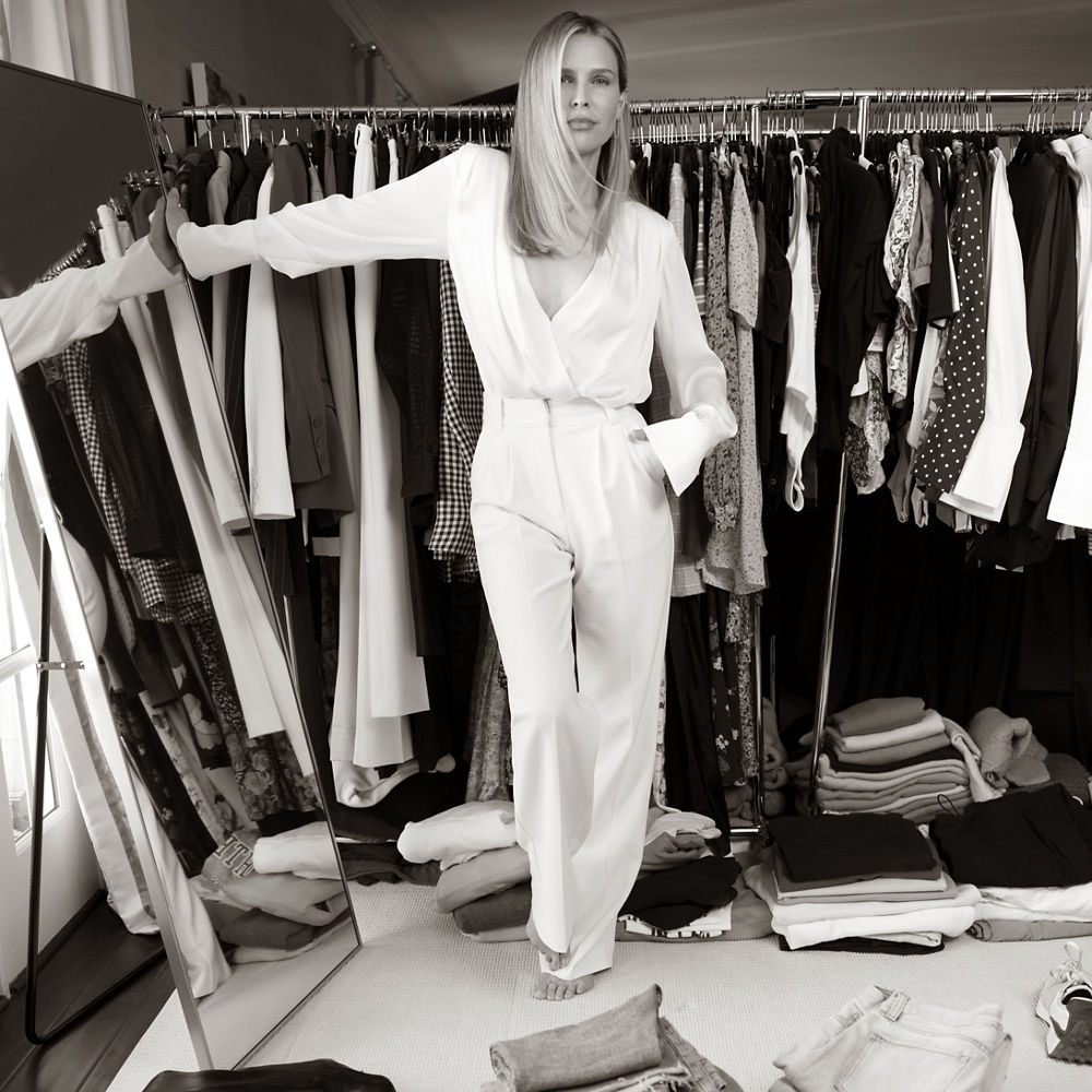 Sara Foster leaning against a vertical mirror while standing in front of a clothes rack.