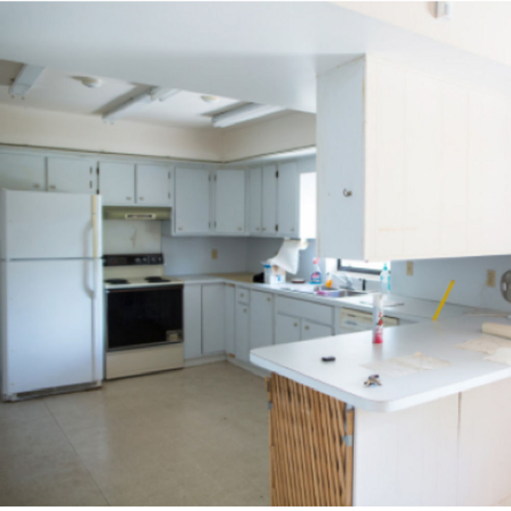 A before photograph of a kitchen with white cabinetry and countertops with a small window.
