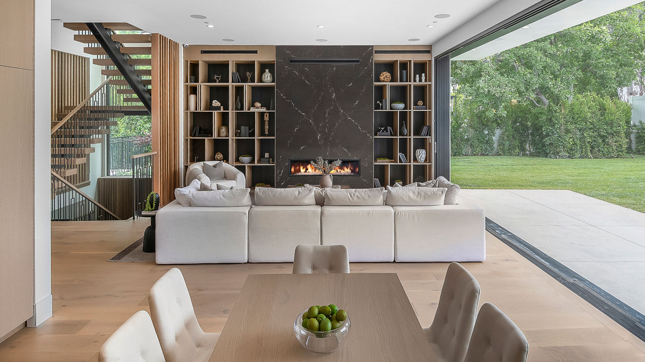 a modern living room with a white sectional sofa, black quartz fireplace, built in bookshelf, and a full-wall window.