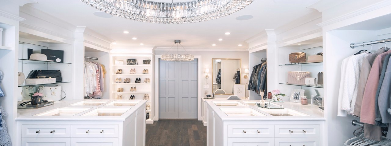 A walk-in closet with identical islands with inset glass panels and jewelry drawers.