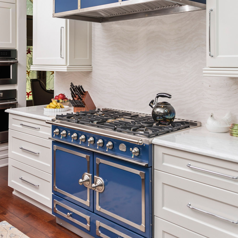a traditional kitchen with white cabinets, white quartz countertops, and a bold blue range and hood with silver buttons and accents