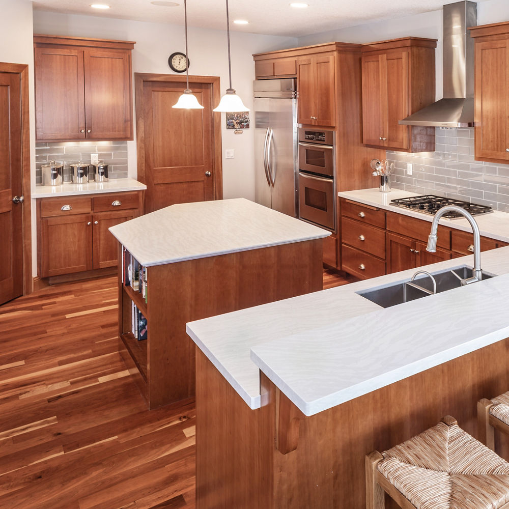 A traditional kitchen with wooden cabinets, white quartz countertops, built-in island, and stainless steal appliances.