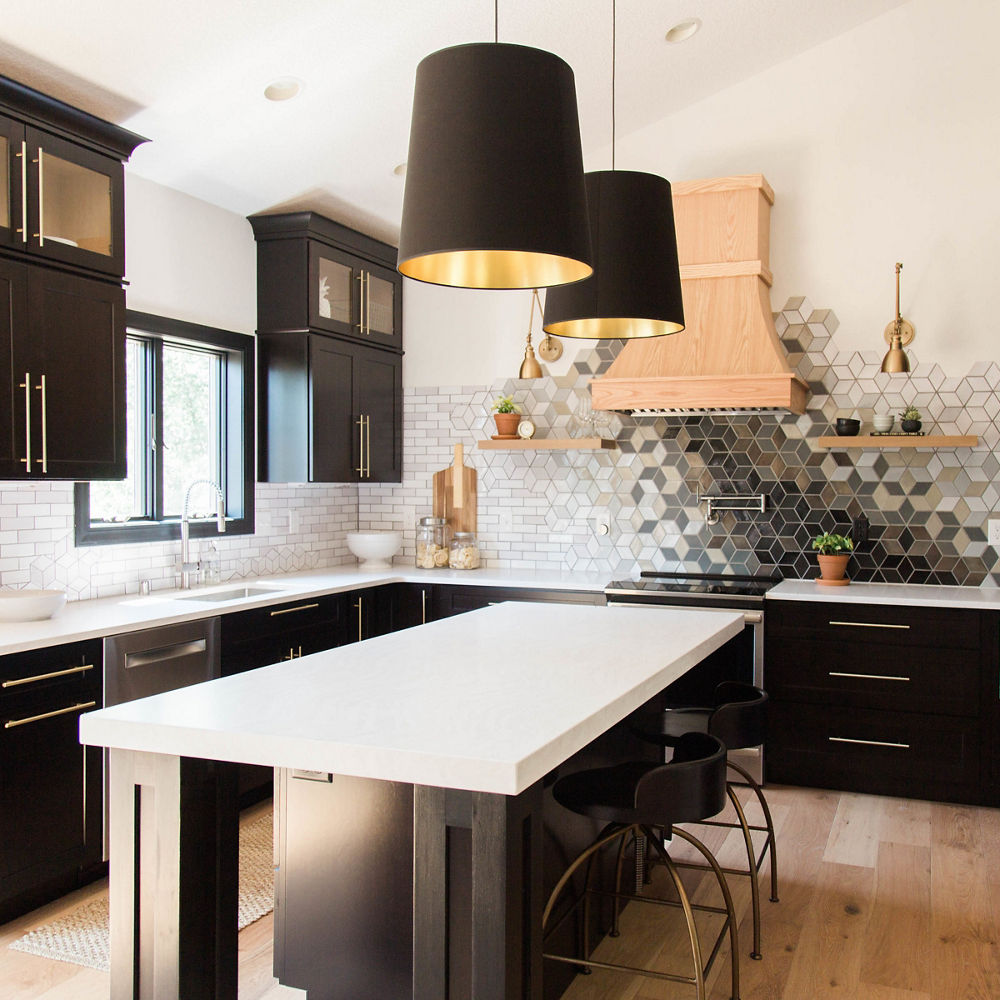 a modern kitchen with black upper and lower cabinets, white quartz countertops, a wooden hood over a sleek range, black pendant lighting, and bold tiled backsplash.